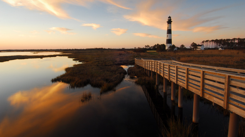 Boardwalk crossing a coastal marsh near a black-and-white lighthouse on Bodie Island, Outer Banks, North Carolina