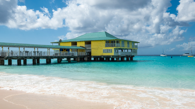 a beautiful white sand beach with a yellow building over it in Barbados