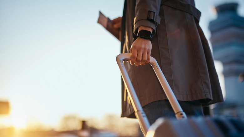 Close-up image of a woman rolling her suitcase and holding travel documents.