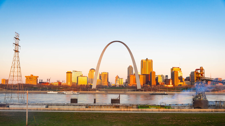 The Gateway Arch at sunset, with buildings in the background and a river in the foreground
