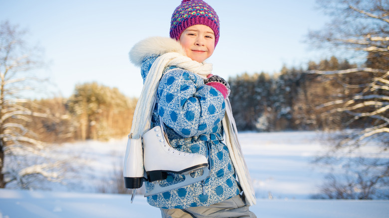Young child holding a pair of ice skates in a snowy landscape