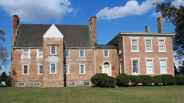 The exterior of Bacon's Castle, with a green lawn and clouds in the blue sky