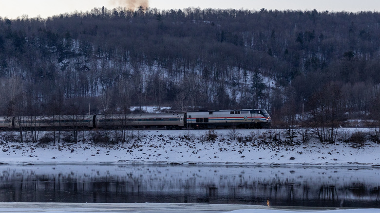 An Amtrak train rides along rails in a winter landscape and with snow on the ground