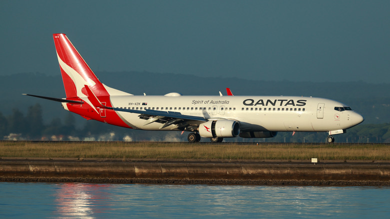 Close up of Qantas airplane landing on a runway with body of water in the foreground.