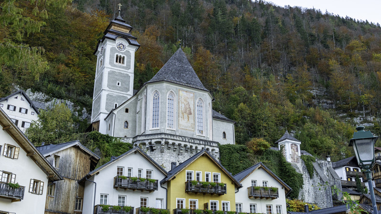 Roman Catholic Parish Church of Hallstatt and colorful houses nestled against a forested mountainside in autumn.
