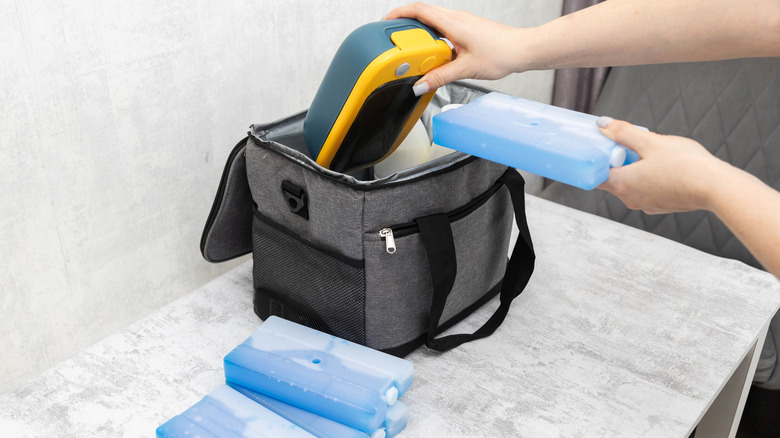 A person's hands arranging a food container and ice pack in a fabric lunch box
