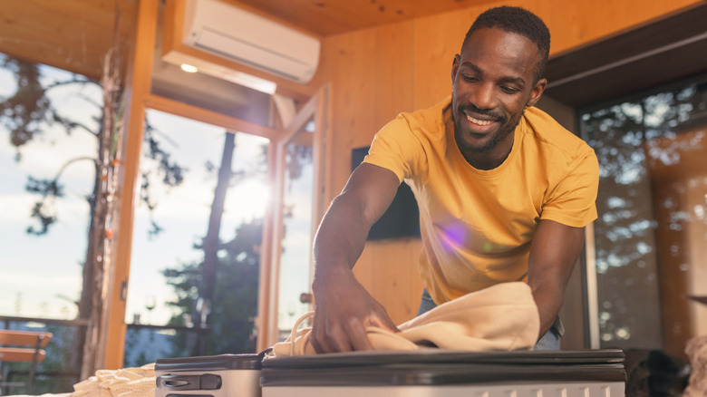 A smiling man packing clothes in a suitcase
