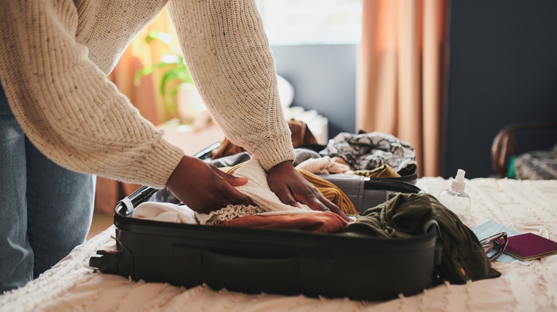 Someone packing a suitcase on a bed