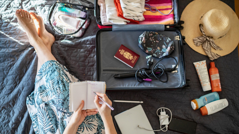 Person sitting on a bed checking their packing list with a notebook and pen