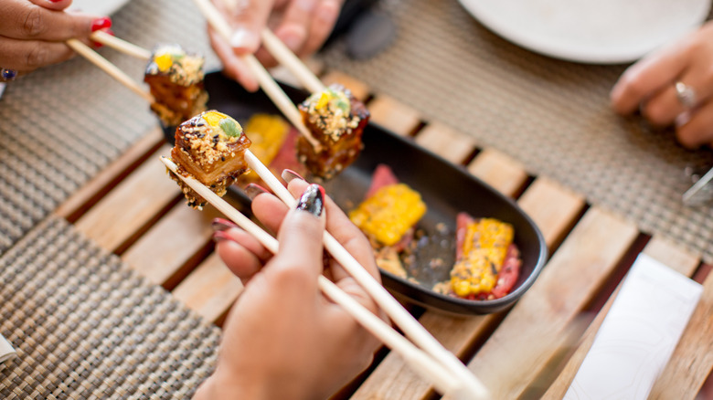 Friends sharing a sushi platter in a restaurant using chopsticks