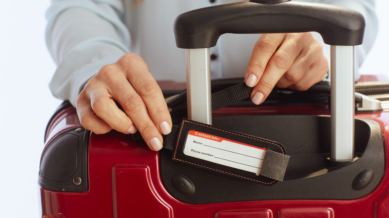 A person attaching a luggage tag on a red suitcase