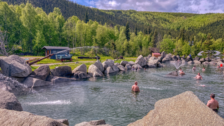 People relaxing in Chena Hot Springs thermal rock pool surrounded by forest near Fairbanks, Alaska