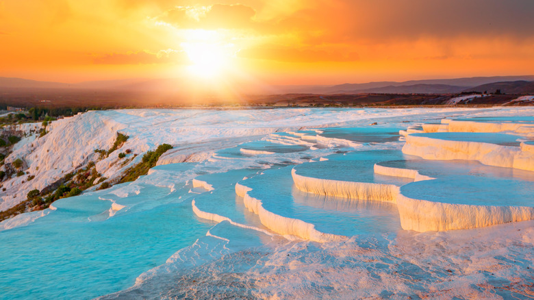 Sun setting over the blue thermal pools and white terraces of Pamukkale, Türkiye