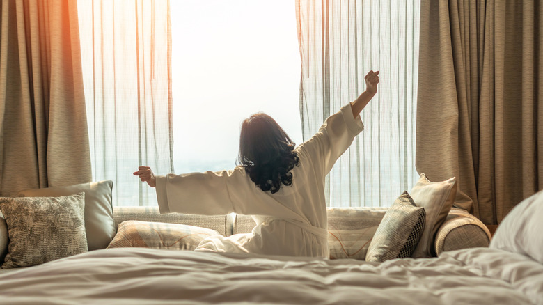 A woman sits and stretches in a luxurious hotel bed