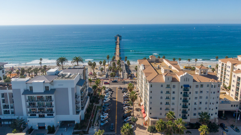 Drone aerial views of downtown Oceanside, California, featuring coastal city streets, beachside hotels, and the iconic Oceanside Pier extending into the Pacific Ocean.