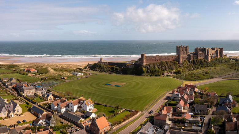Aerial landscape panorama view of Bamburgh castle and a village cricket pitch on the Northumberland coast