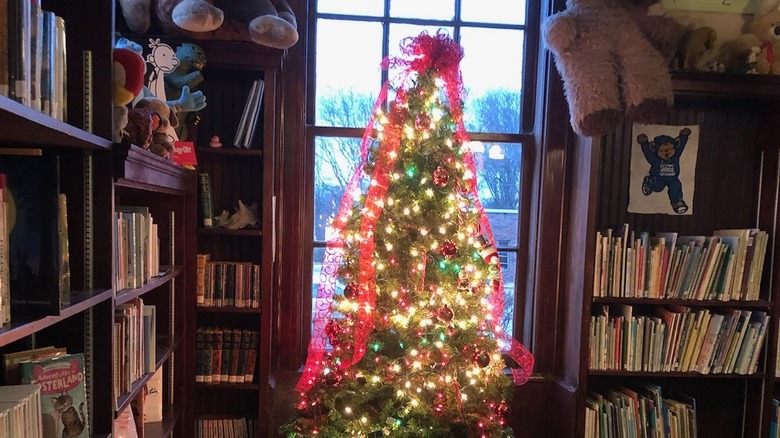 a christmas tree illuminates the interior of the library and shelves full of books