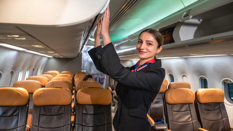 Caucasian female flight attendant closing overhead compartment security checking on board