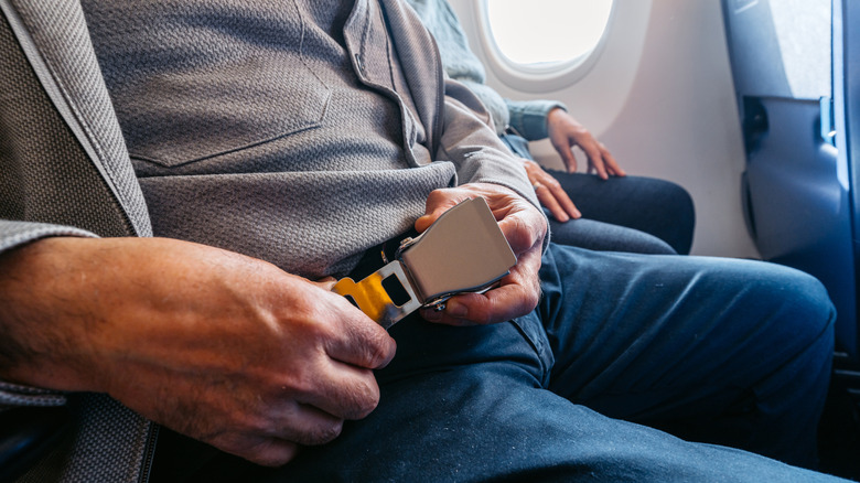 A closeup of a man fastening his seatbelt on an airplane.
