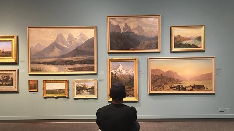 A man looks at a wall of several Canadian landscape paintings at Glenbow Museum