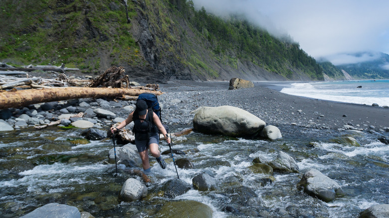A woman crossing a river with trekking poles on the Lost Coast Trail in California