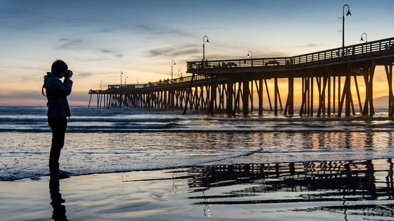 A man taking a picture of the Pismo Beach Pier at sunset