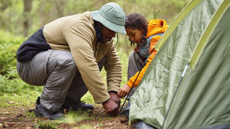 A man and child setting up a camp tent in the forest.