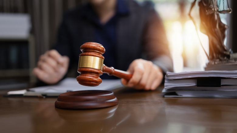 A person holding a gavel hammer with a document on a table