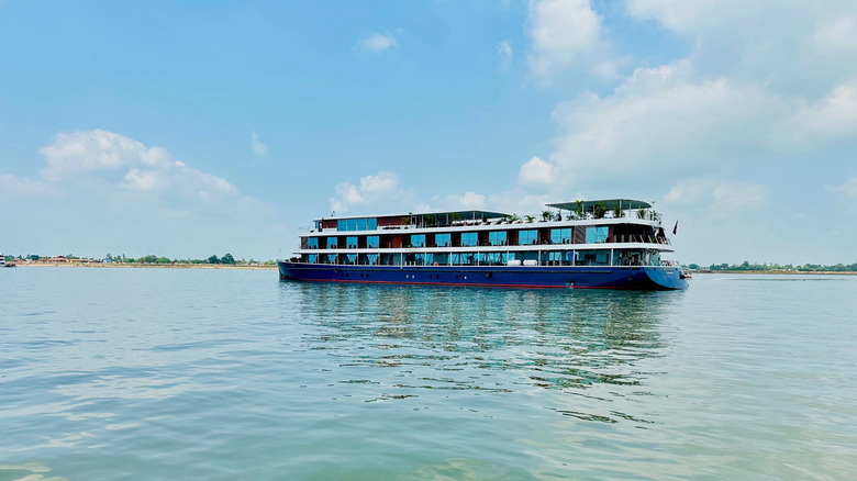 Small blue river cruise boat on the green expanse of the Mekong River in Cambodia