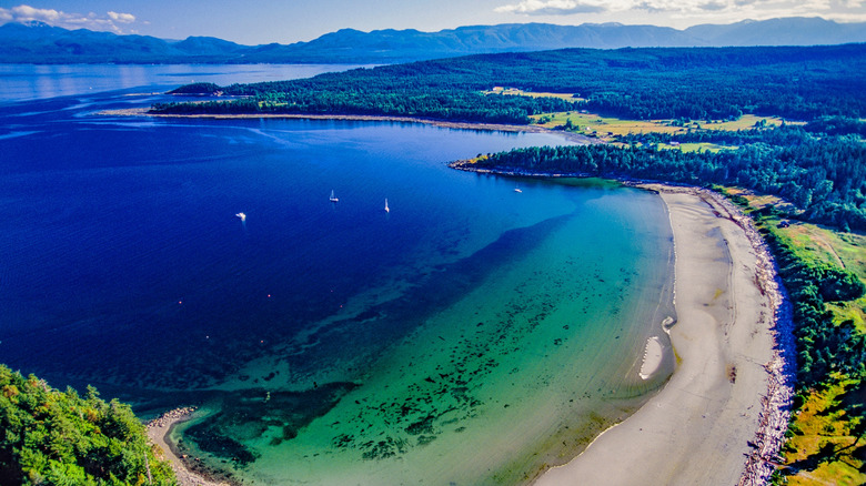 Aerial view of a white sand beach and surrounding bay near distant mountains on Hornby Island, BC, Canada