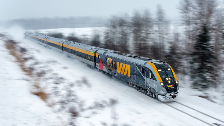 a Via Rail train moving along snowy tracks with trees in background