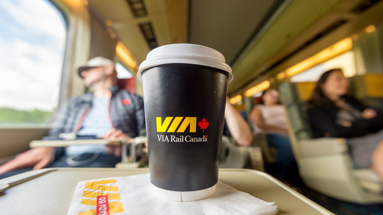 Close up of VIA Rail branded coffee up on tray table with passengers in the background.