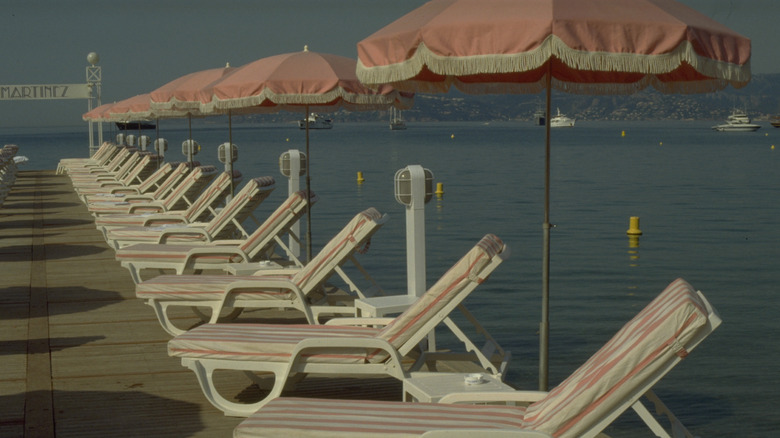 Pink and white striped beach loungers and pink umbrellas with yachts in the background at Plage du Martinez, Cannes, France