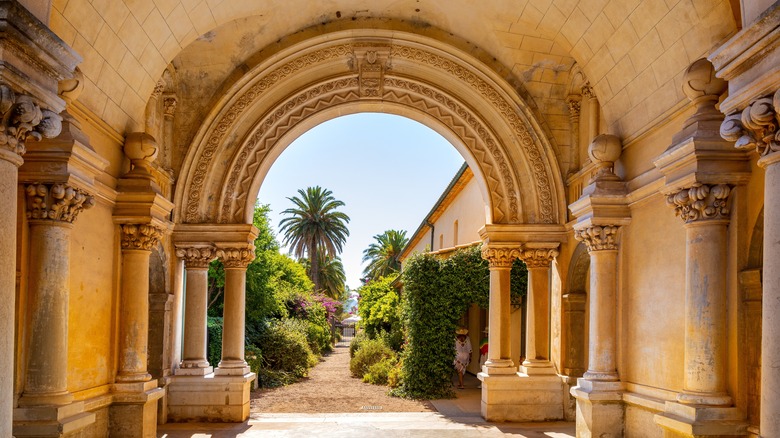 Ornate arched cloisters of the Abbey de Lerins monastery on Saint-Honorat Island with palm trees and gardens visible through the arched opening