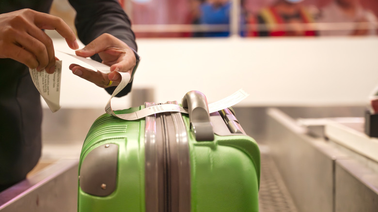 A green suitcase is labeled by an airline staff member at a check-in counter.