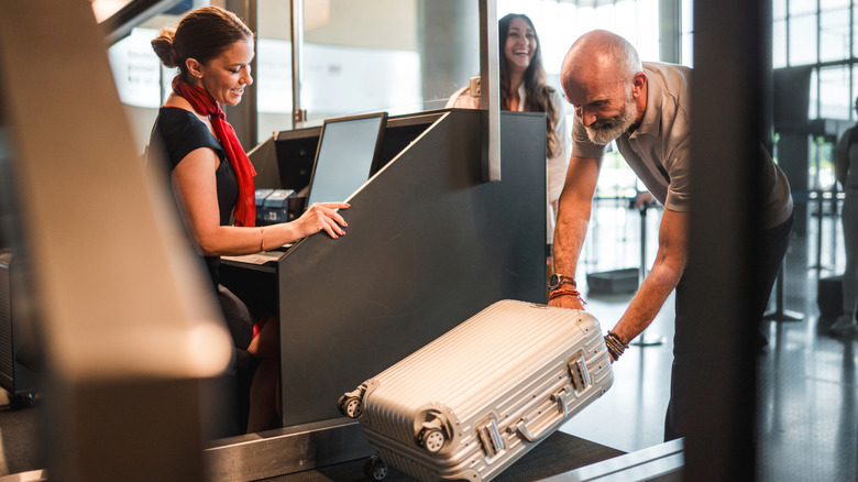 A man loads a piece of luggage onto the scale at airport check-in.