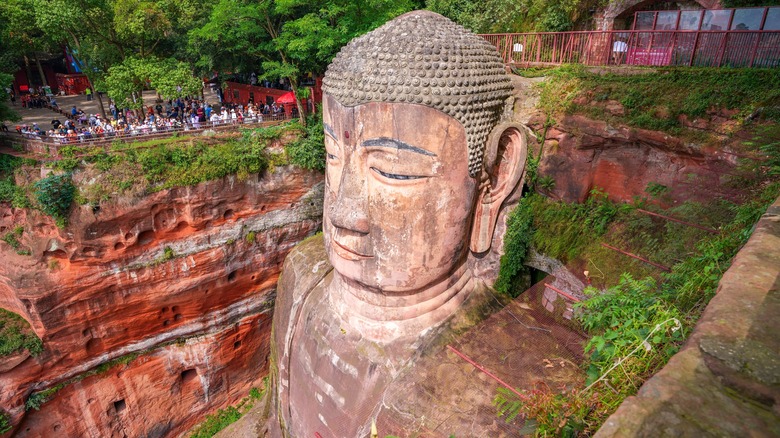 People look over a cliff at the Leshan Giant Buddha sculpture