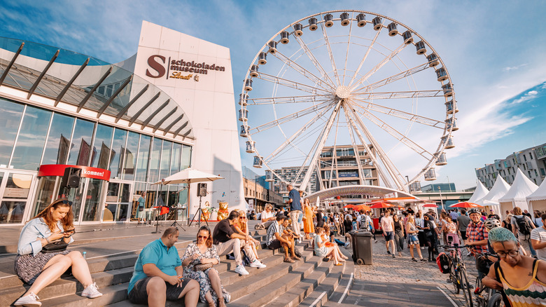 People sit outside of the Chocolate Museum near a ferris wheel in Cologne