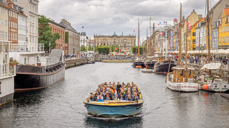 Boat filled with tourists on tour of Copenhagen's canal, lined with boats and historic buildings