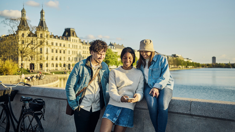 Three people stand near a bike on a bridge overlooking Copenhagen's canal at sunset