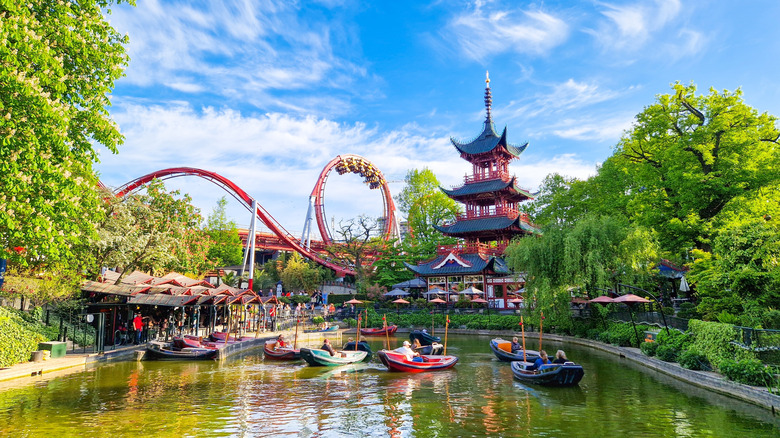 Copenhagen's historic amusement park, Tivoli Gardens, with a boat-filled pond, Chinese pagoda, and rollercoaster, on a sunny spring day