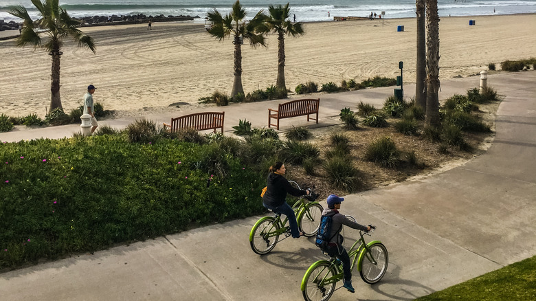two people on bikes along a boardwalk next to the beach