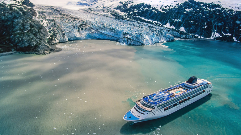 Aerial view of cruise ship in turquoise water surrounded by Alaska's snowy mountains.