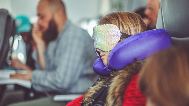 A woman with an eye mask and shoulder rest on a plane