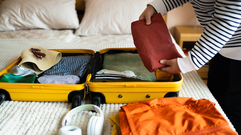A person placing items in an open suitcase on a bed