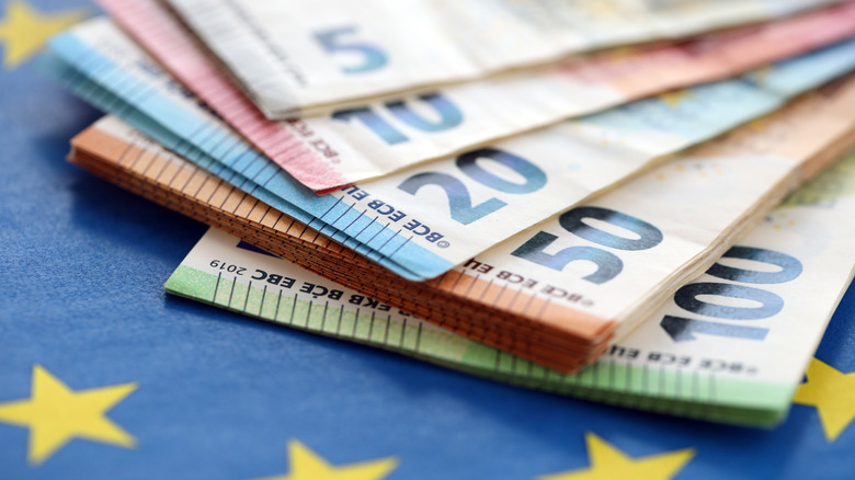 Different Euro bills fanned out on an EU yellow and blue flag