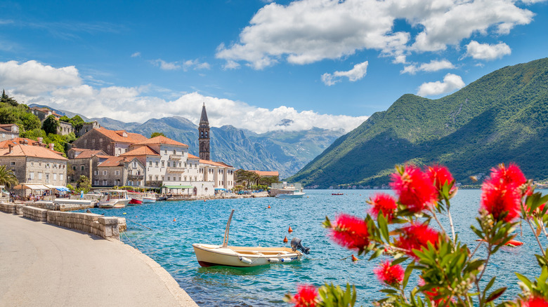 Perast on the Bay of Kotor framed by dramatic mountains, a boat, and red flowers