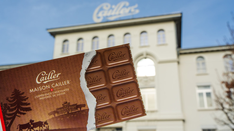 Cailler chocolate bar in front of a white ornate building of the historic Cailler Chocolate Factory in Broc, Switzerland