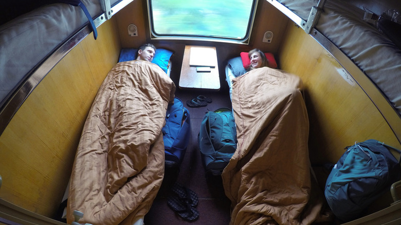 Couple lying in bed under the warm blankets while riding in a sleeper train.