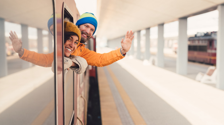 Young man with girlfriend waving with hand from the train